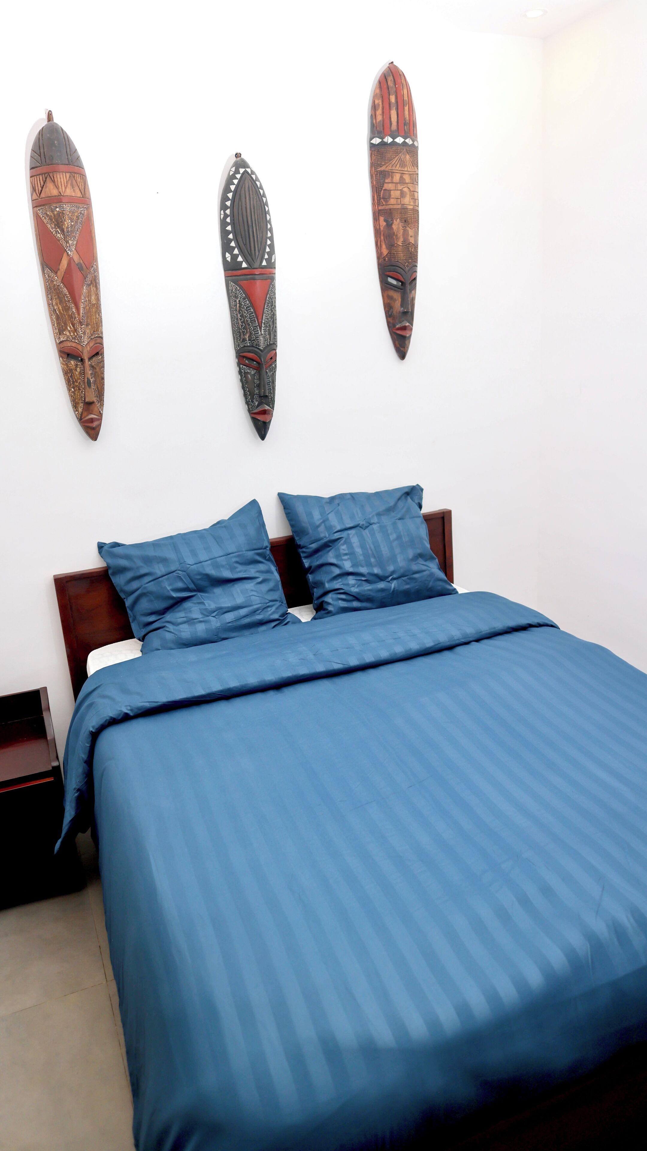 A bed with blue bedding, a wooden headboard, and three wall-mounted decorative items.