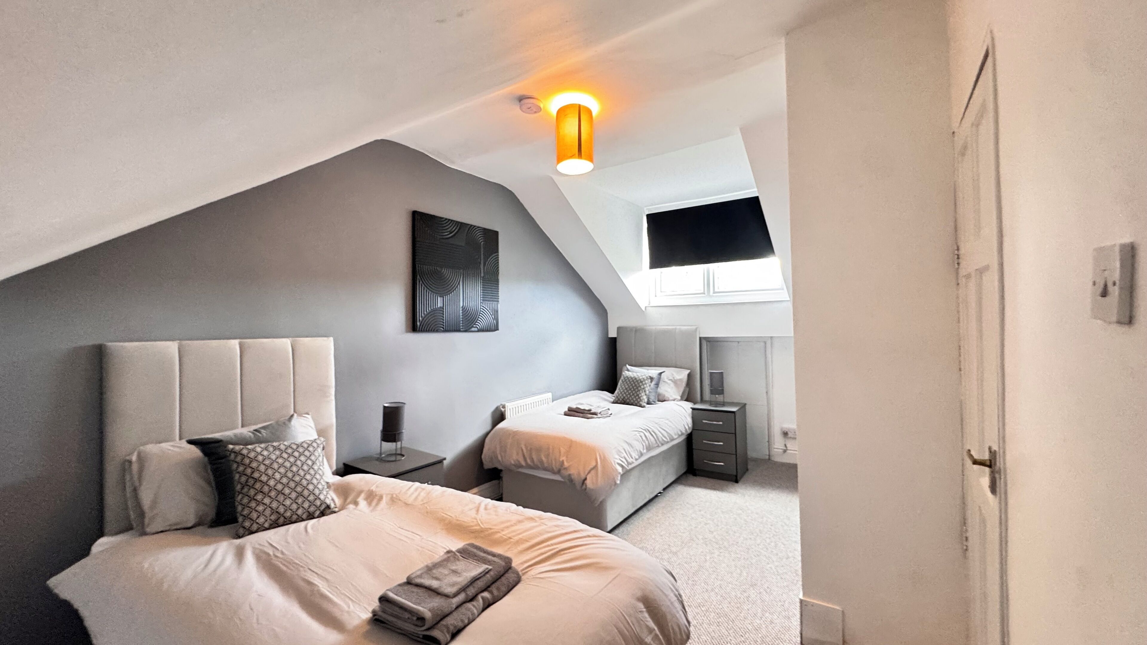 A modern bedroom with a sloped ceiling, two beds, a desk, and a large window.