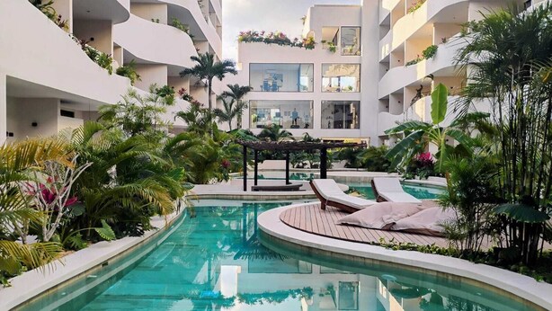 Et moderne hotel med central pool, omgivet af frodigt grønt og flere altaner med planter.