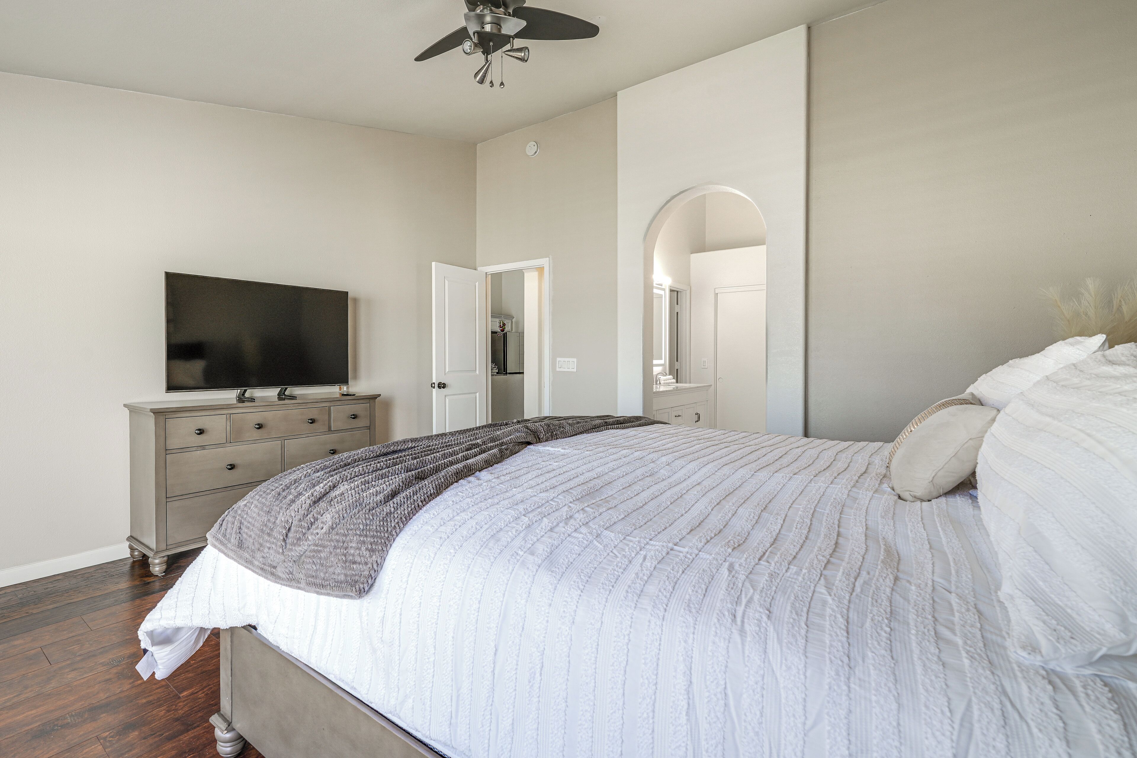 A bedroom with a bed, a dresser, a television, and a ceiling fan.