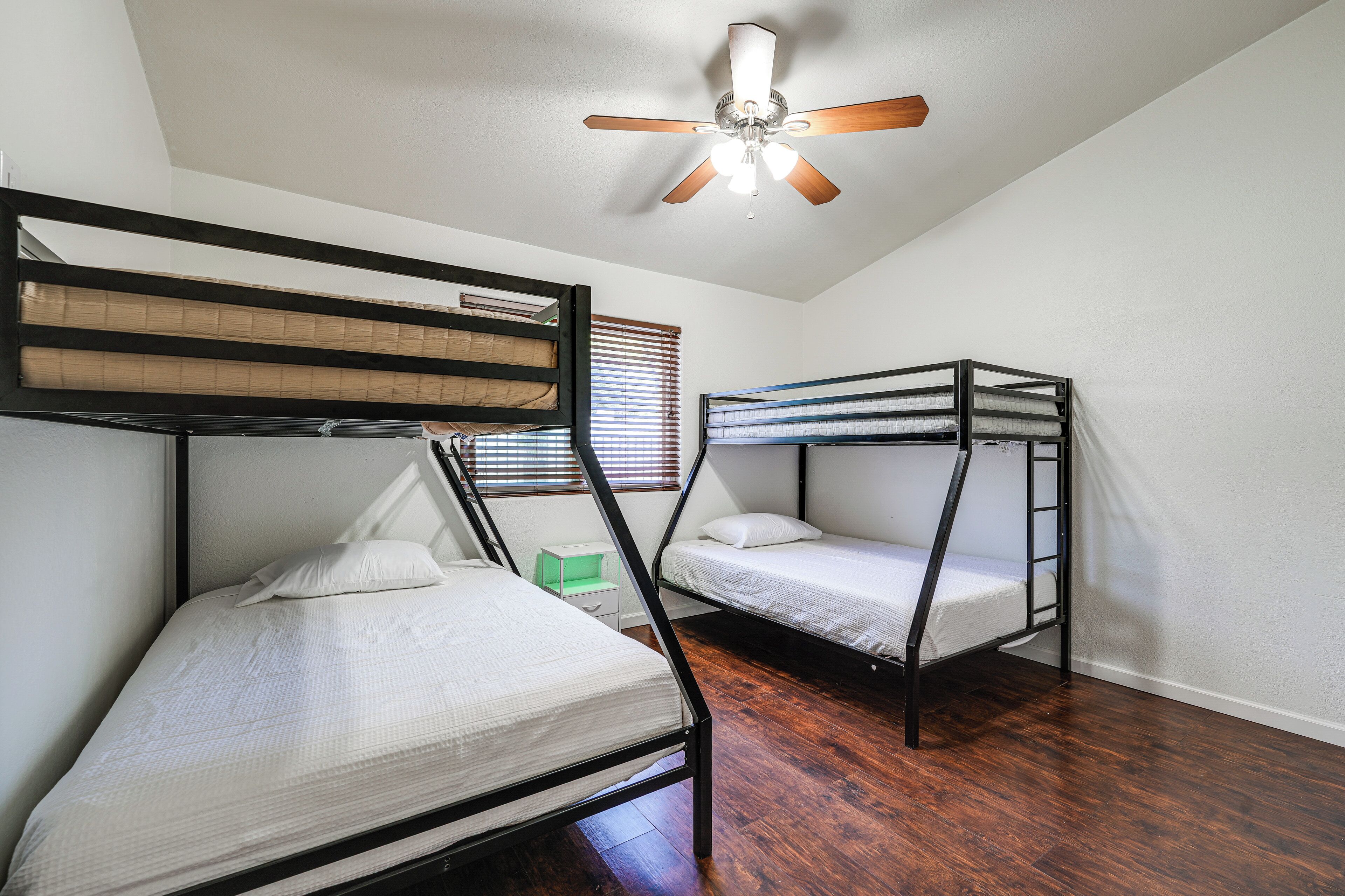 A dormitory room with bunk beds, a ceiling fan, and a window with blinds.