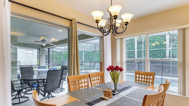 A dining area with a table set for six, surrounded by chairs, a chandelier, and a vase with red flowers. - 11 Mi to Disney! Family Haven w/ Poolside Oasis (Davenport)