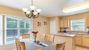 A dining area with a table set for six, surrounded by wooden chairs, a chandelier, and a view of greenery outside. - 11 Mi to Disney! Family Haven w/ Poolside Oasis (Davenport)