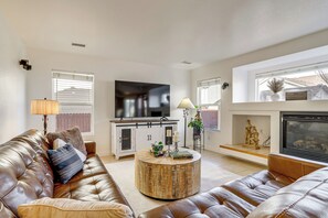 A living room with a leather sofa, a round coffee table, a flat-screen TV, and a fireplace. - 9 Mi to Dia: Group Getaway w/ Easy Denver Access (Commerce City)