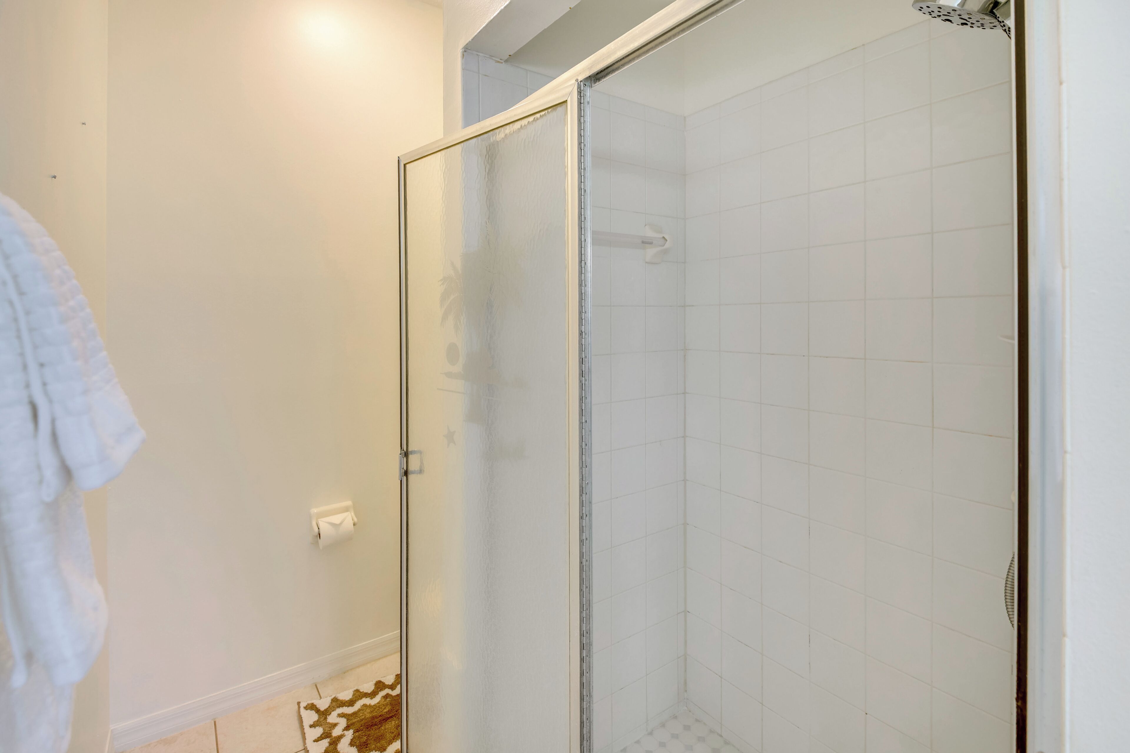 A bathroom with a glass-enclosed shower, white tiled walls, and a visible towel rack.