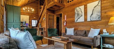 A log cabin interior with a wooden staircase, a dining area, and a living room with a sofa and a coffee table.