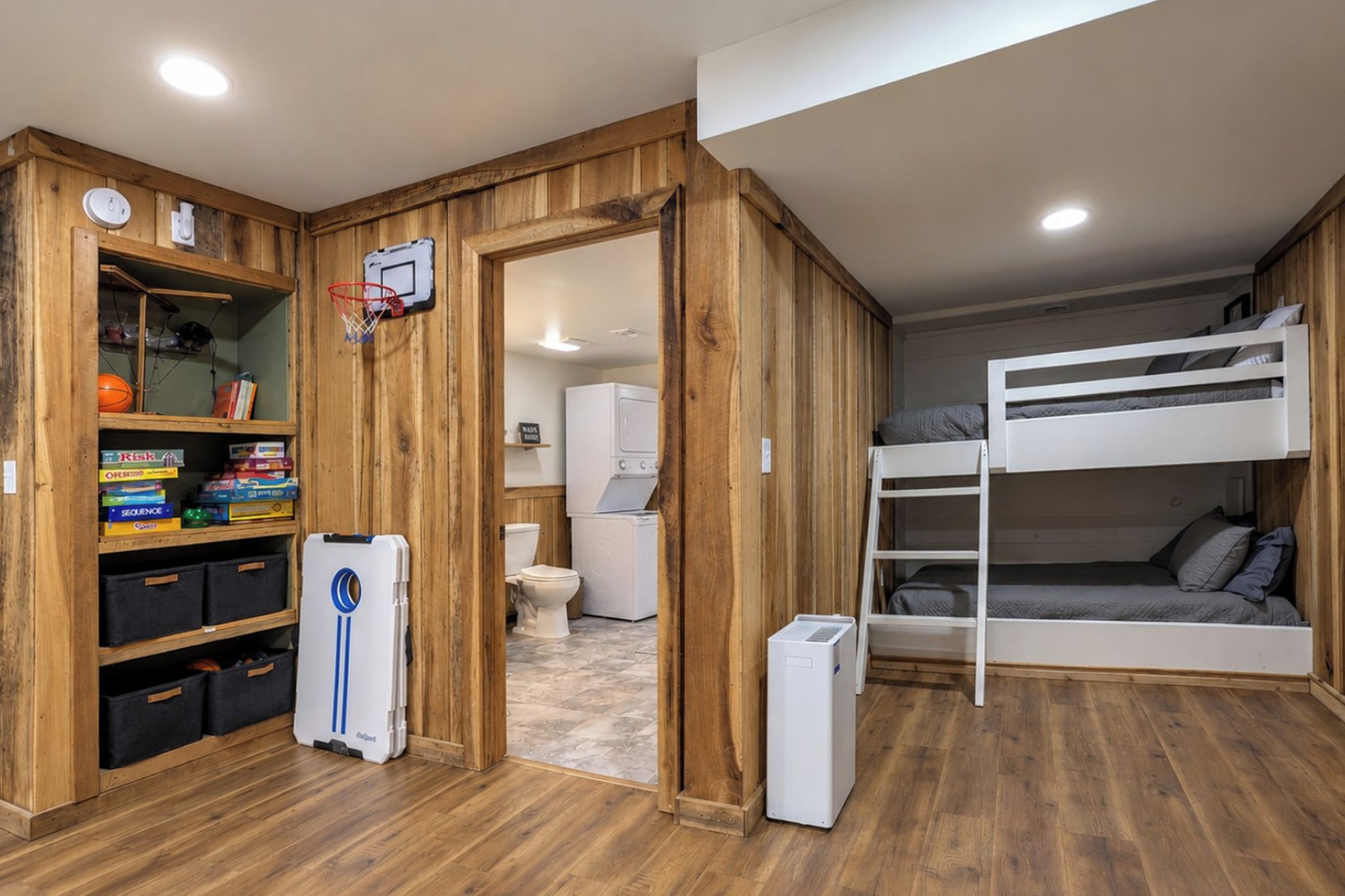 Una stanza compatta con un letto a castello, pareti in legno, un angolo cottura e un mobile contenitore con giochi.