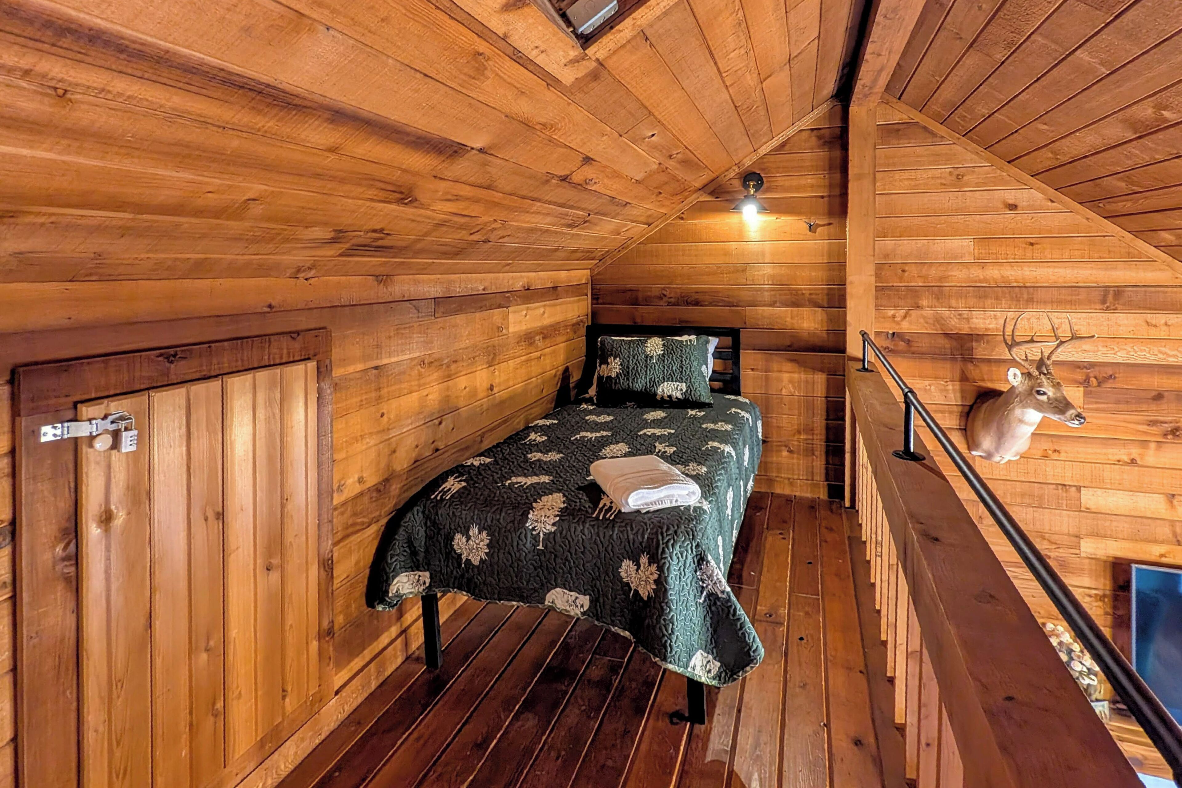 A wooden cabin room with a bed, a mounted deer head, and a staircase.