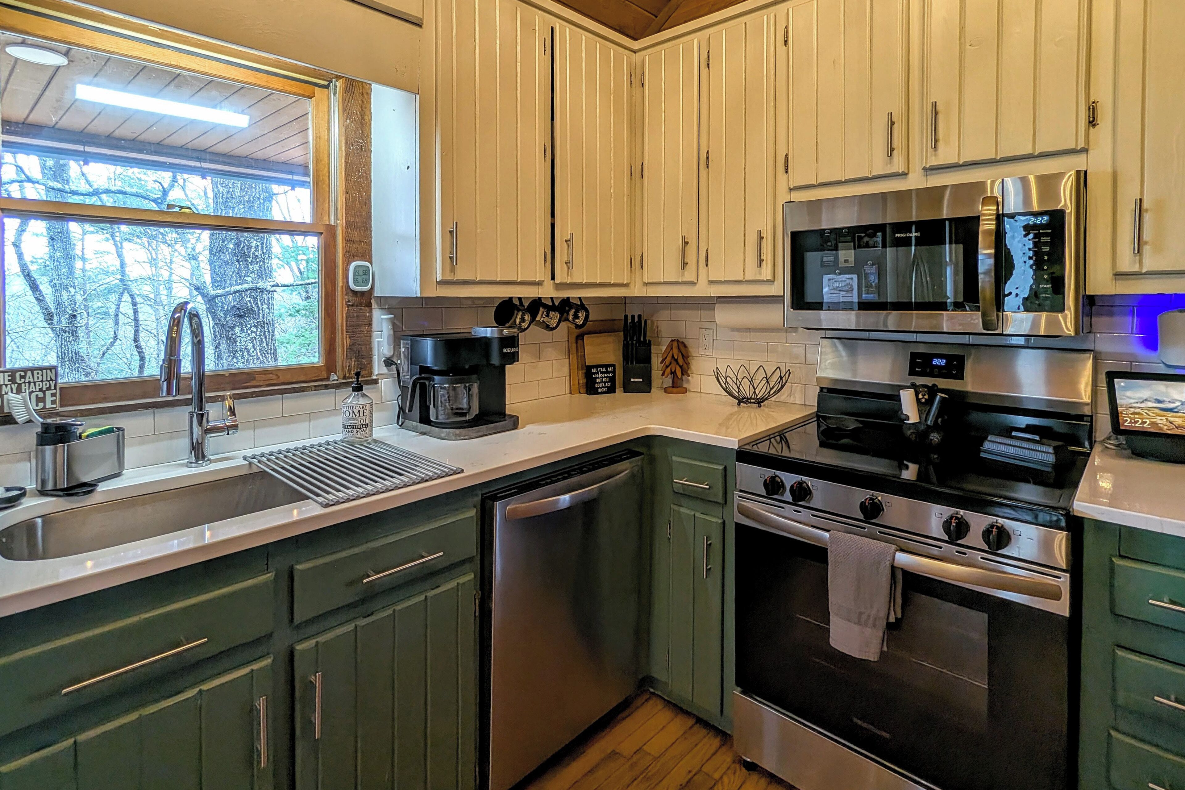 A modern kitchen with a dishwasher, stove, microwave, and a window with a view of trees.