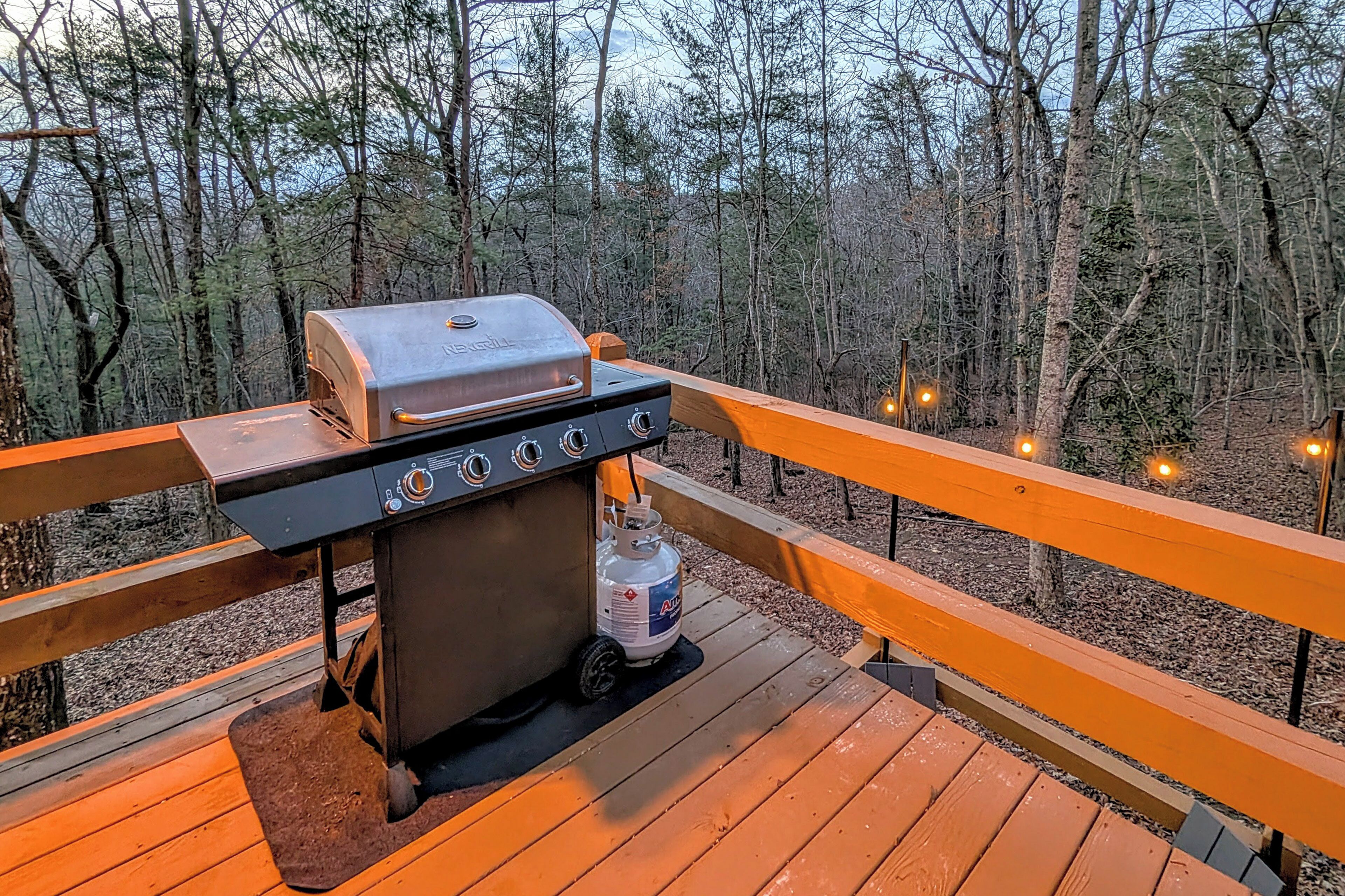 A barbecue grill on a wooden deck with a view of a forest.