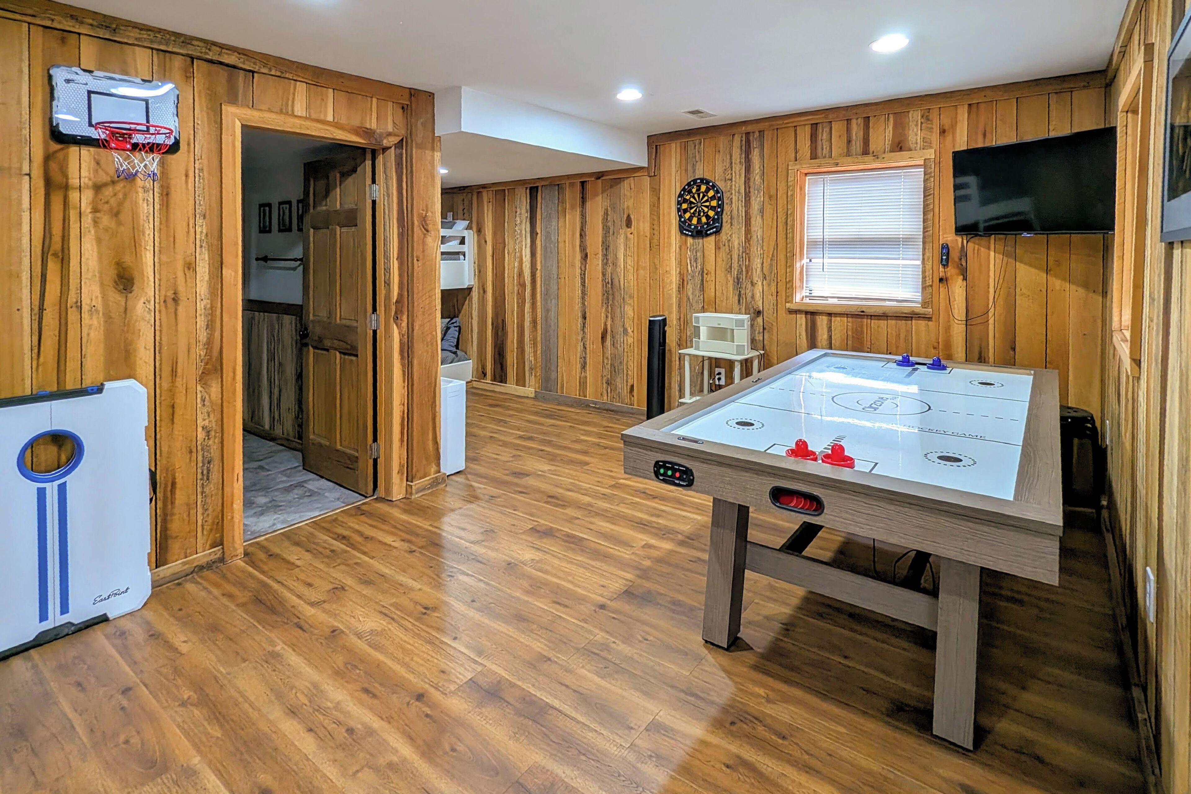 Een kamer met een tafelvoetbaltafel, een dartbord, een aan de muur bevestigde televisie en een basketbalring.