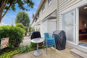 Eine Terrasse mit Tisch und Stühlen, einem überdachten Grill und einer Flagge.