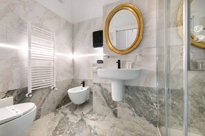 A modern bathroom with a marble floor, a white toilet, a bidet, a pedestal sink, a gold-framed mirror, and a glass shower enclosure. - King Deluxe Segantini Room for Small Groups and Families (Lecco)