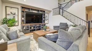 Una sala de estar moderna con sofás grises, una mesa de centro de madera y un televisor de pantalla plana grande.
