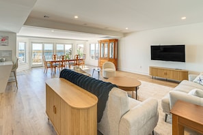 A spacious living area with a large window overlooking the sea, a wooden cabinet, a flat-screen TV, and a cozy seating arrangement. - Private Pool, Dock & Beach: Stafford Township Gem (Manahawkin)