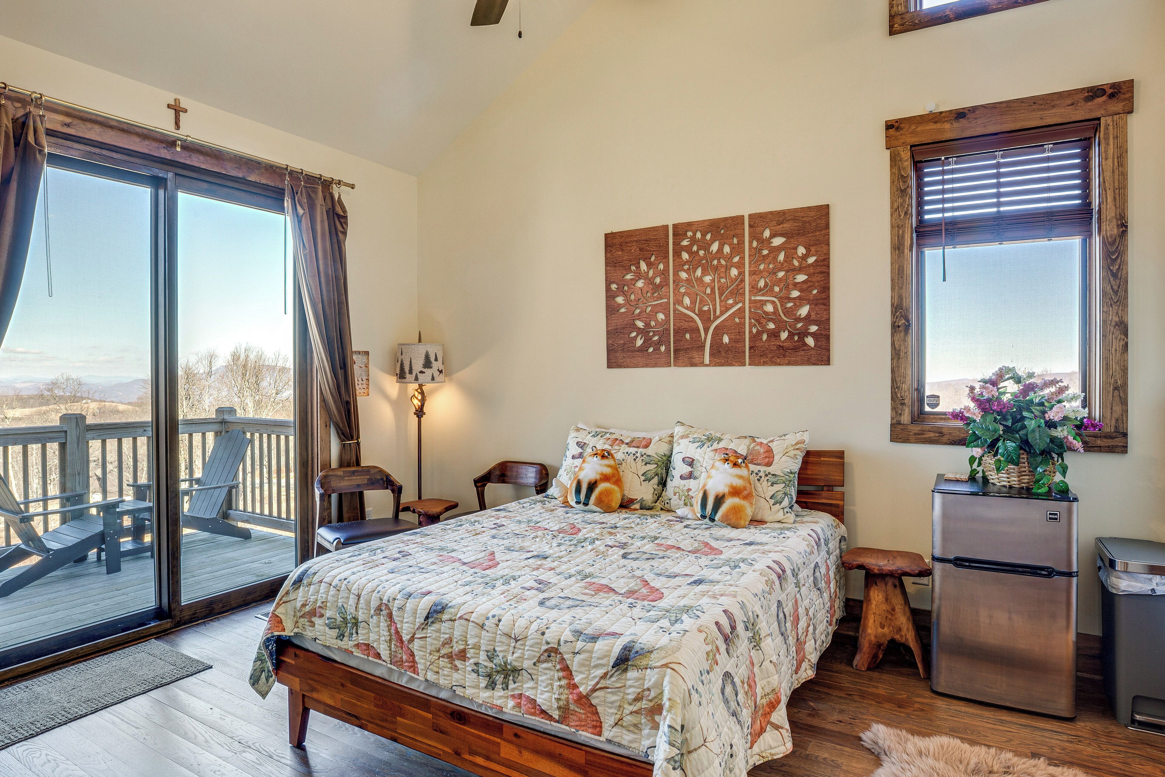 Une chambre avec un grand lit, une tête de lit en bois, un petit tabouret, un réfrigérateur et une vue sur l’extérieur grâce à une porte-fenêtre coulissante.