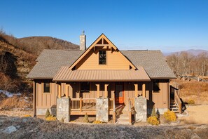 A wooden cabin with a stone chimney, a porch with wooden railings, and a view of the surrounding hills. - A Piece of Heaven: Long Range Mtn Views All Year! (Banner Elk)