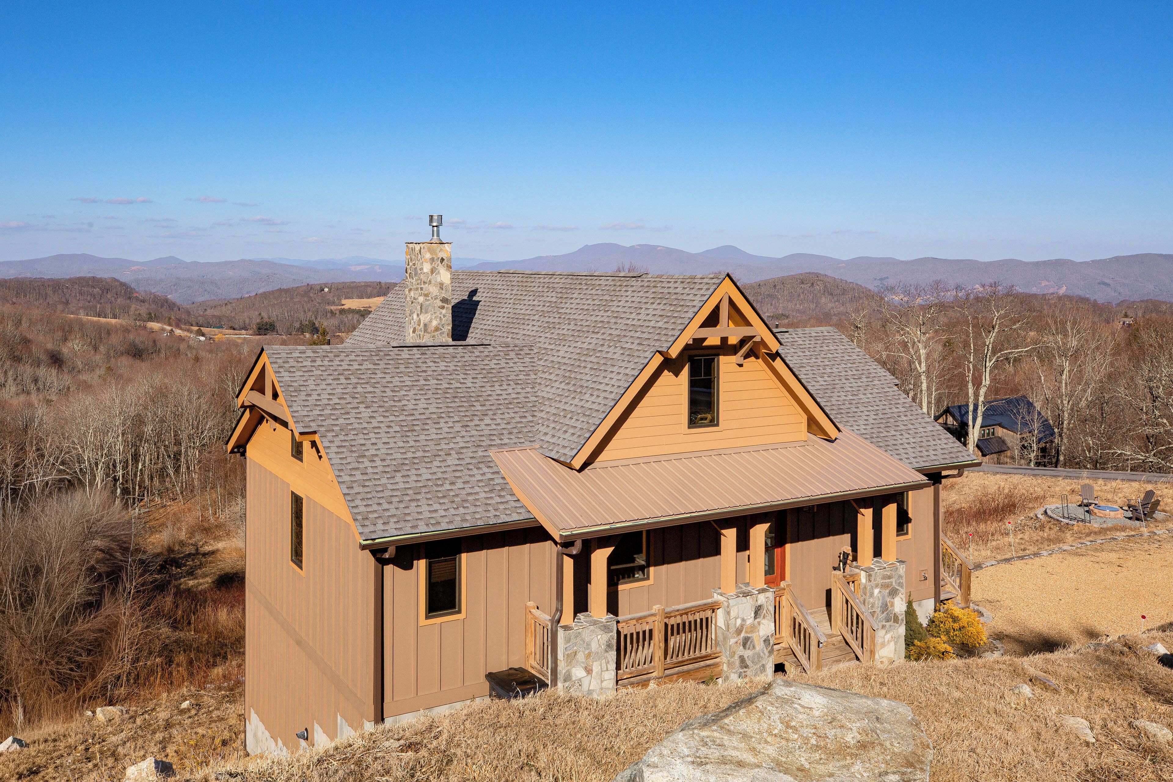 A wooden cabin with a stone chimney, a porch, and a view of the surrounding mountains.