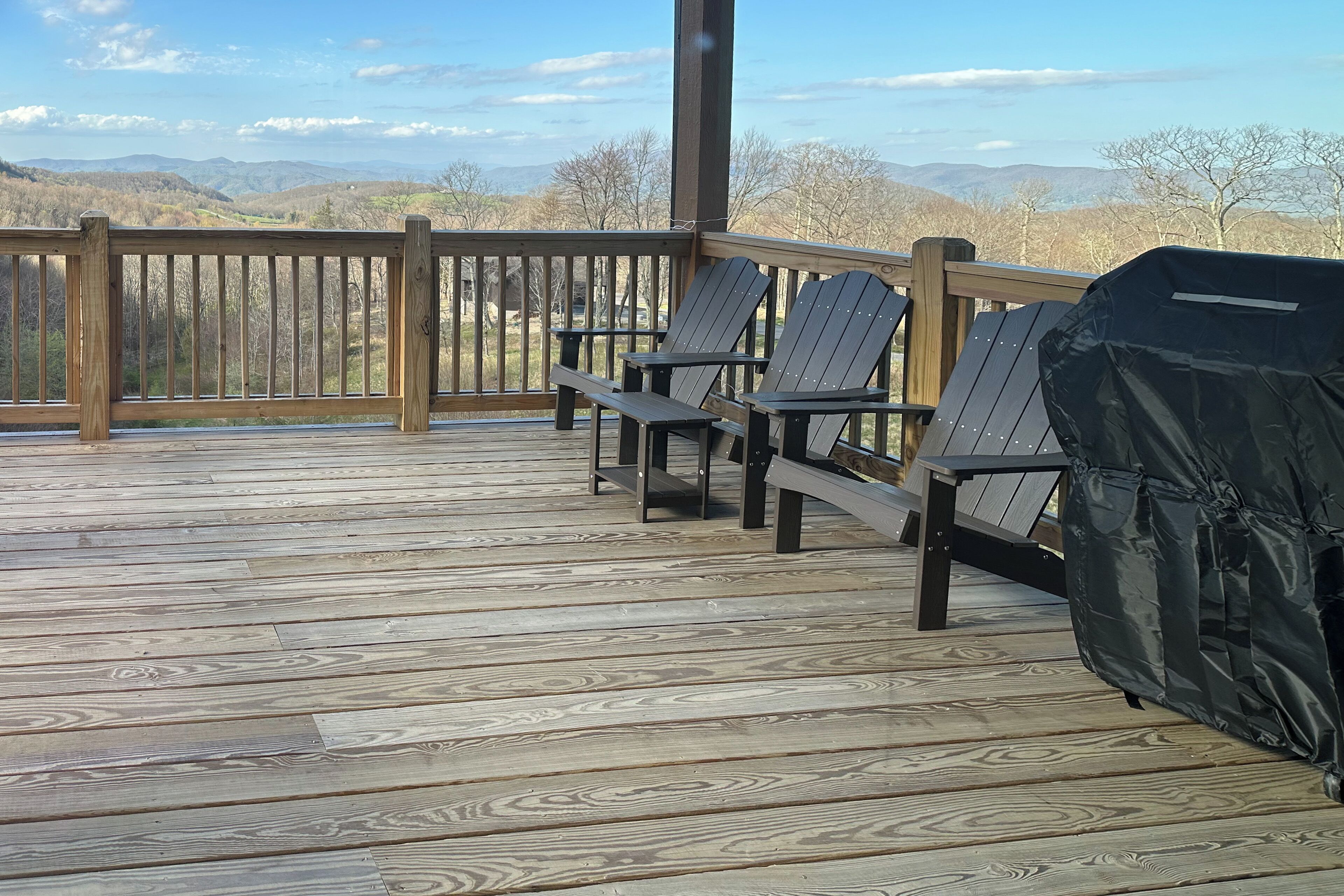 Una terraza de madera con sillas Adirondack y una parrilla.