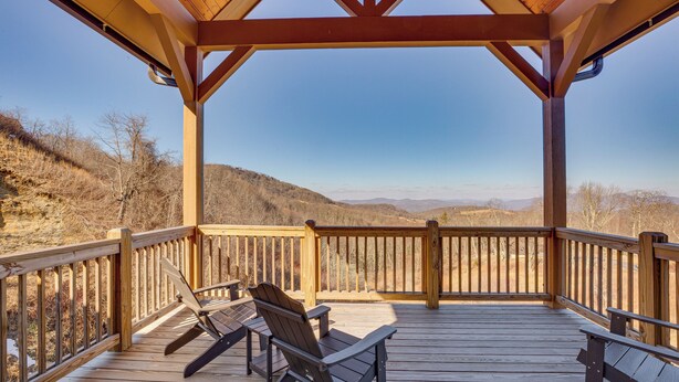 Une terrasse en bois avec deux fauteuils Adirondack, une pergola et une vue sur un paysage montagneux.