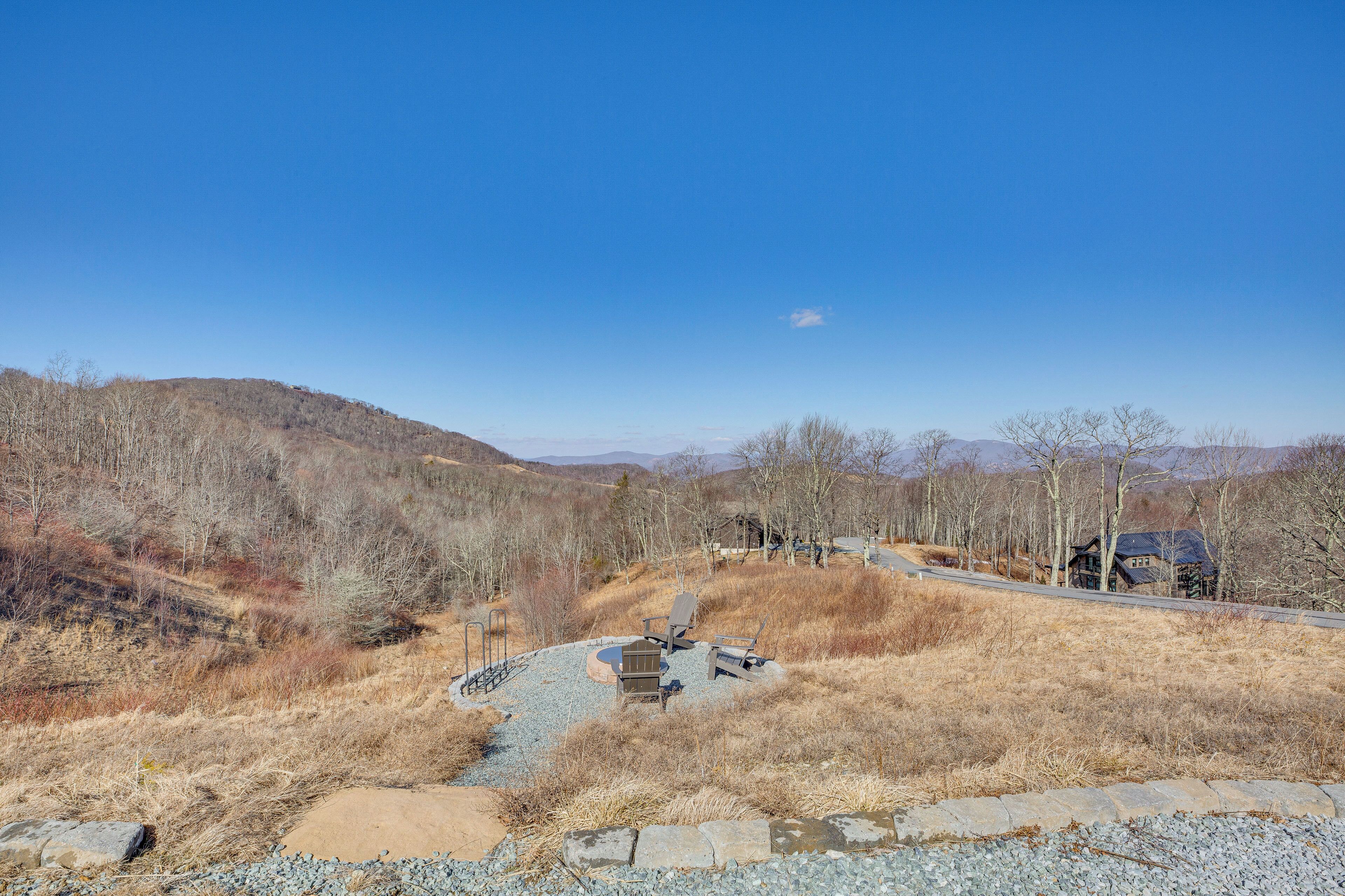 A rustic cabin with a stone fireplace and outdoor seating, surrounded by dry grass and trees, with a clear blue sky above.