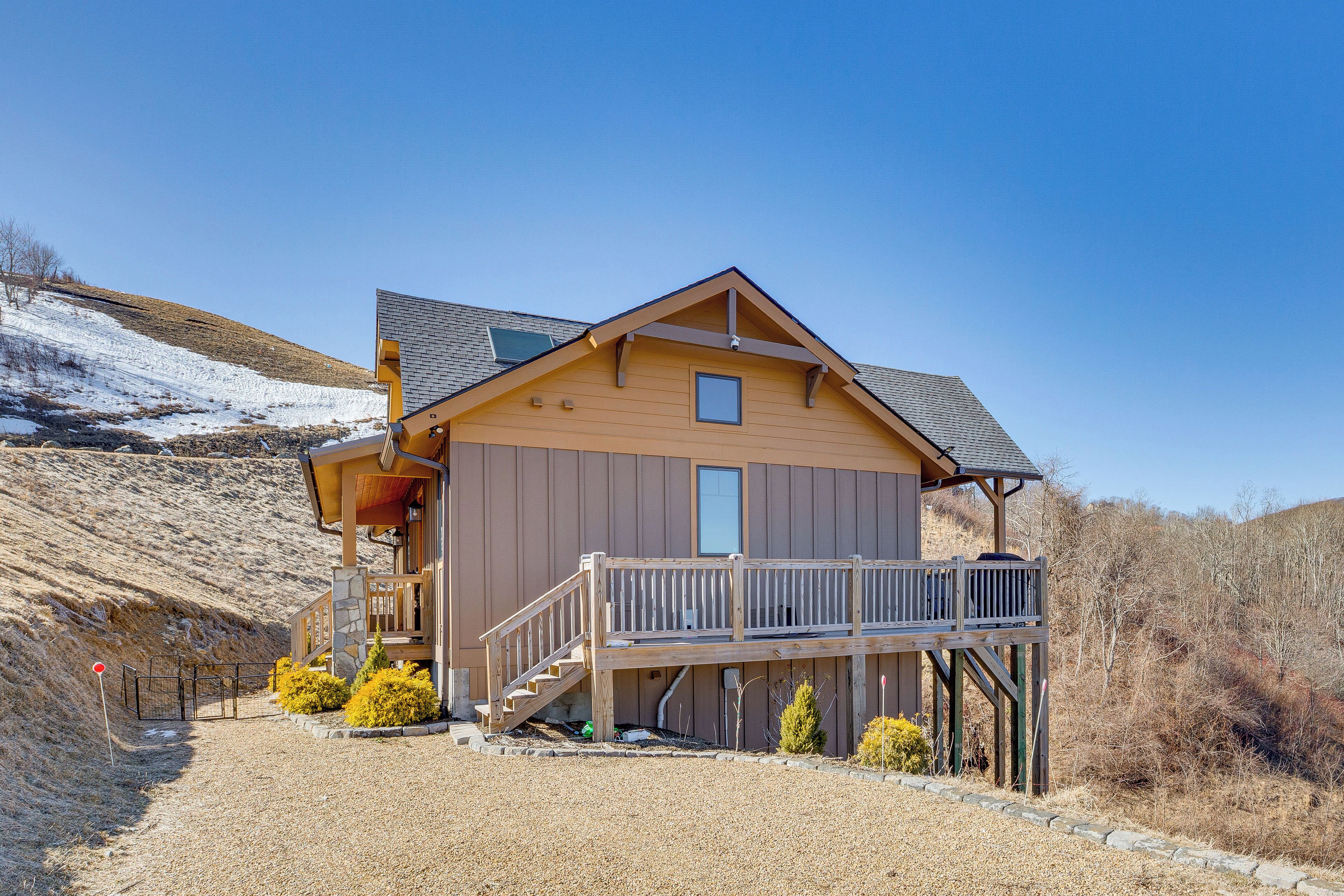 A two-story wooden cabin with a balcony, a stone foundation, and a clear sky.