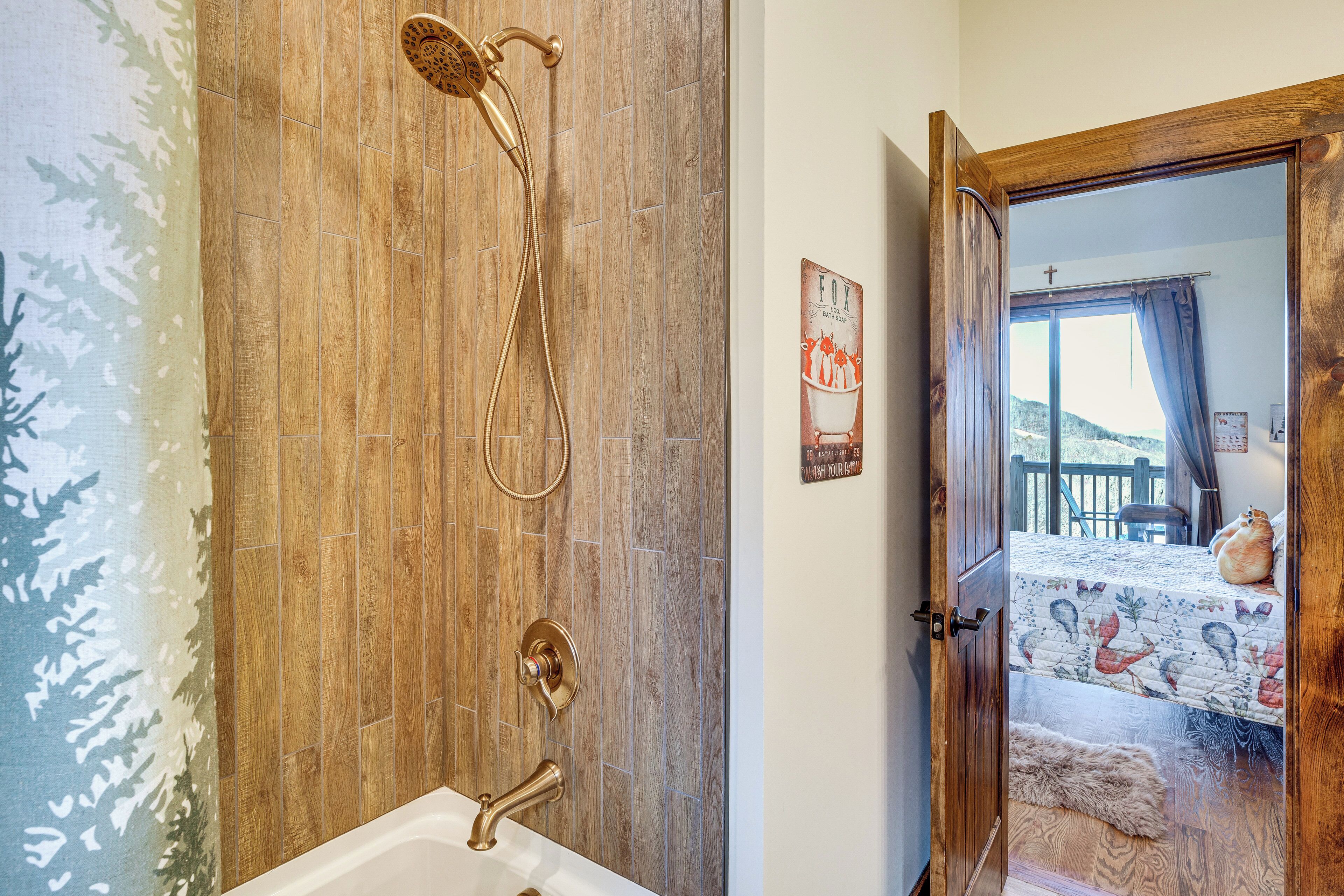 Un baño con cabina de ducha de madera, una bañera y una puerta que da a un dormitorio con cama y vistas al exterior.