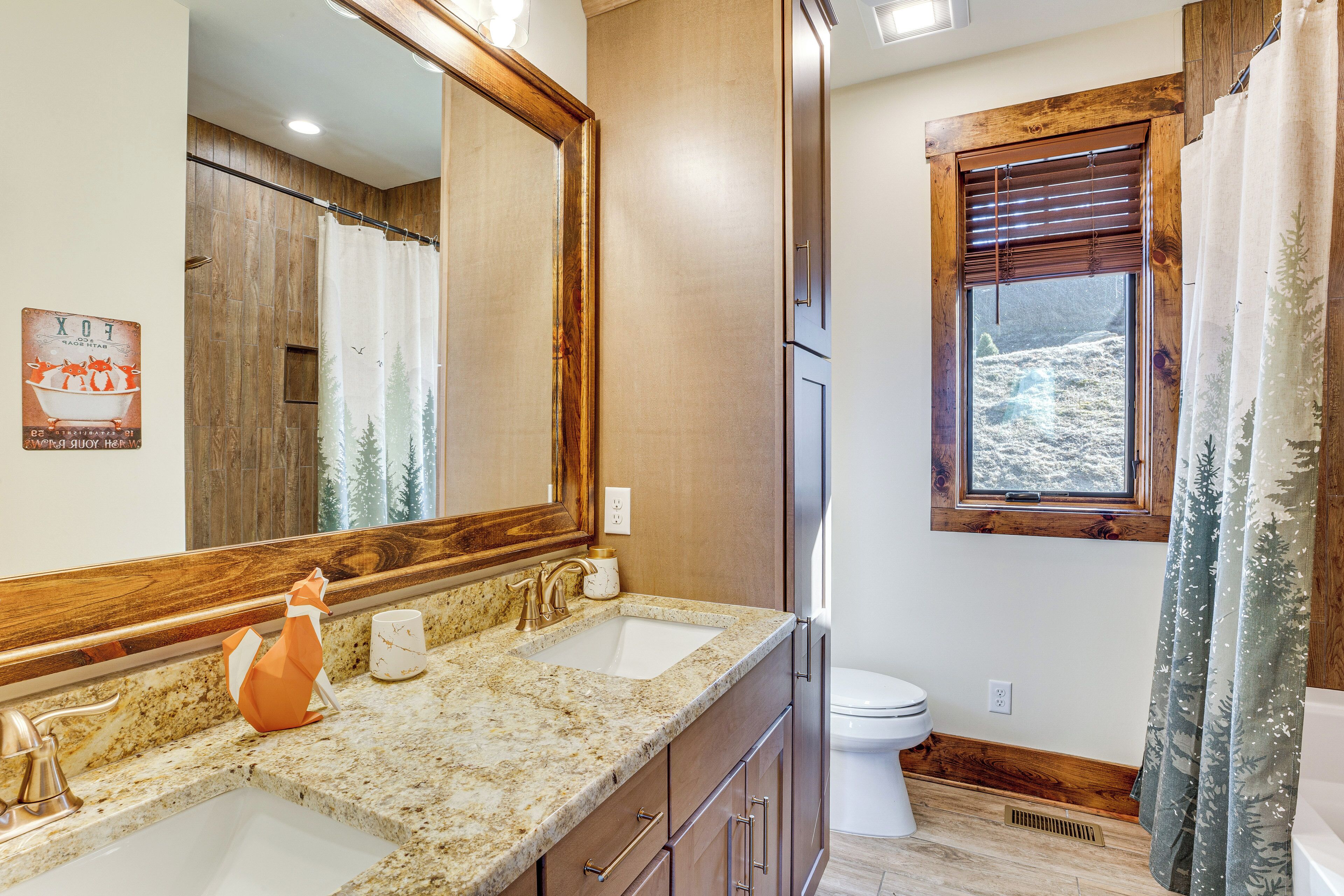 A bathroom with two sinks, a large mirror, a toilet, and a window with a view of a rocky landscape.