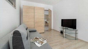 A modern living room with a grey sofa, a glass TV stand, and a wooden wardrobe. - Functional Apartment with Balcony | Quiet Neighborhood (Kraków)