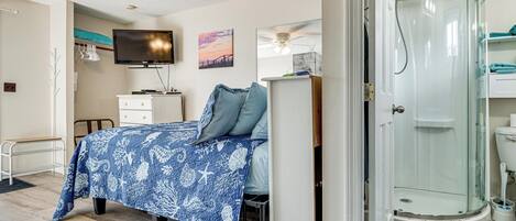 A bedroom with a bed, a TV, a desk, and a shower.