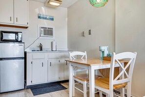A compact kitchen with white cabinets, a microwave, a refrigerator, and a dining table with white chairs. - Steps to Sandy Beach! Oceanfront Old Orchard Gem (Old Orchard Beach)