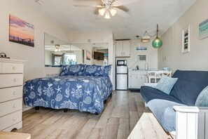 A bedroom with a bed, a dresser, a nightstand, a ceiling fan, and a kitchenette area with a refrigerator and microwave.