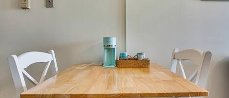 Une table en bois avec des chaises, une bouteille d’eau de couleur turquoise et un panier rempli de tasses.