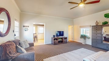 A spacious living room with a ceiling fan, a large mirror, a gray sofa, a white rug, and a TV on a wooden stand.