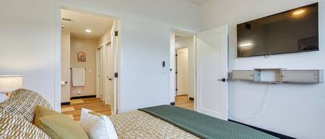 Une chambre d’hôtel avec un lit, un plaid vert, un téléviseur à écran plat et un couloir menant à une autre pièce.