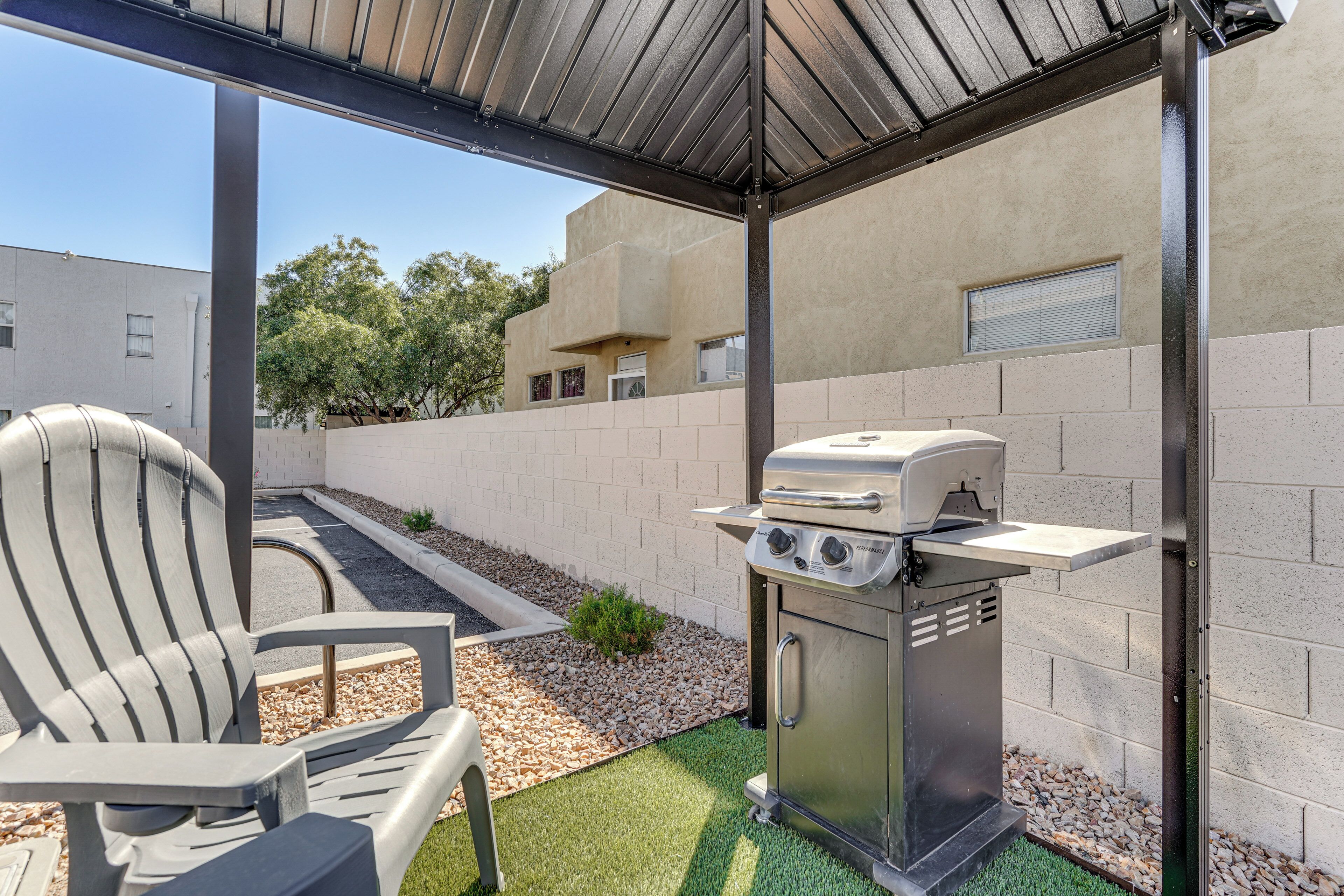 A covered outdoor area with a grill, a chair, and a small garden bed.