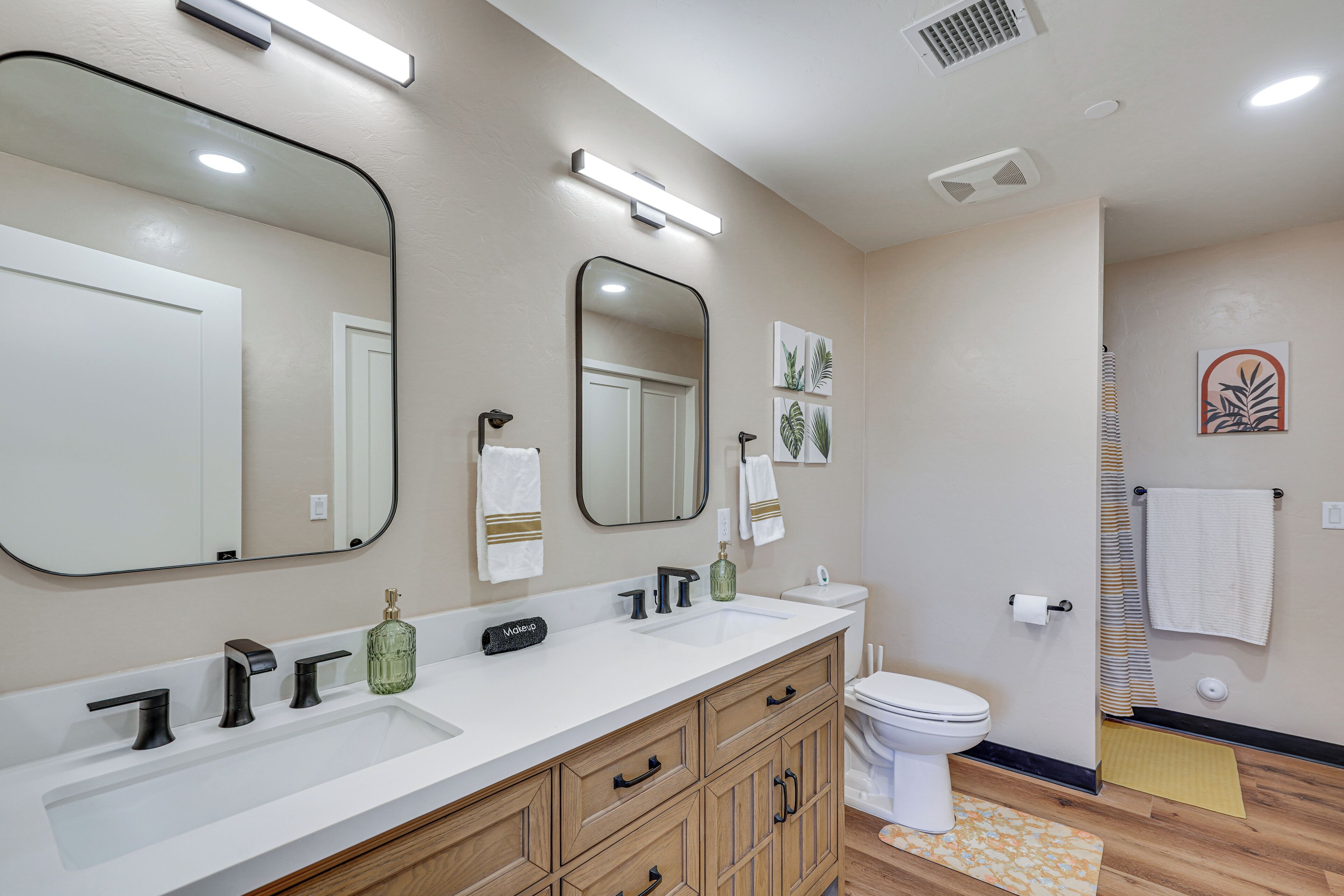 A bathroom with a white sink, two mirrors, a toilet, and wooden cabinets.