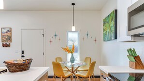 Une cuisine moderne avec un coin repas, comprenant une table à plateau en verre, des chaises jaunes, un panier posé sur le comptoir et un vase rempli de fleurs.