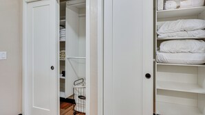 Un placard blanc, dont les portes sont ouvertes et qui révèle des étagères et un espace pour suspendre des vêtements, ainsi qu’un panier à linge et un interrupteur visible.