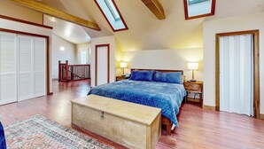 Um quarto amplo com uma cama grande, vigas de madeira no teto, claraboias e vista para uma escadaria.