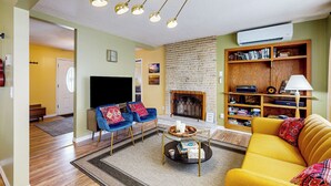 Uma sala de estar com um sofá amarelo, poltronas azuis, lareira e uma estante de livros.