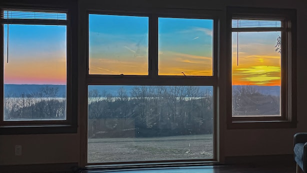 Quarto com quatro janelas grandes que oferecem vista para uma paisagem nevada e um pôr do sol.