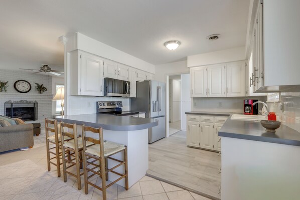 A modern kitchen with white cabinets, a central island with bar stools, a microwave, and a refrigerator.