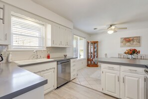 A modern kitchen with white cabinets, a dishwasher, and a dining area with a vase of flowers.