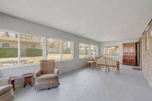 A spacious room with large windows, a wooden bench, a cushioned chair, and a small table.