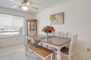 A dining area with a wooden table, benches, and chairs. There is a vase with flowers on the table. A ceiling fan is visible above the table.