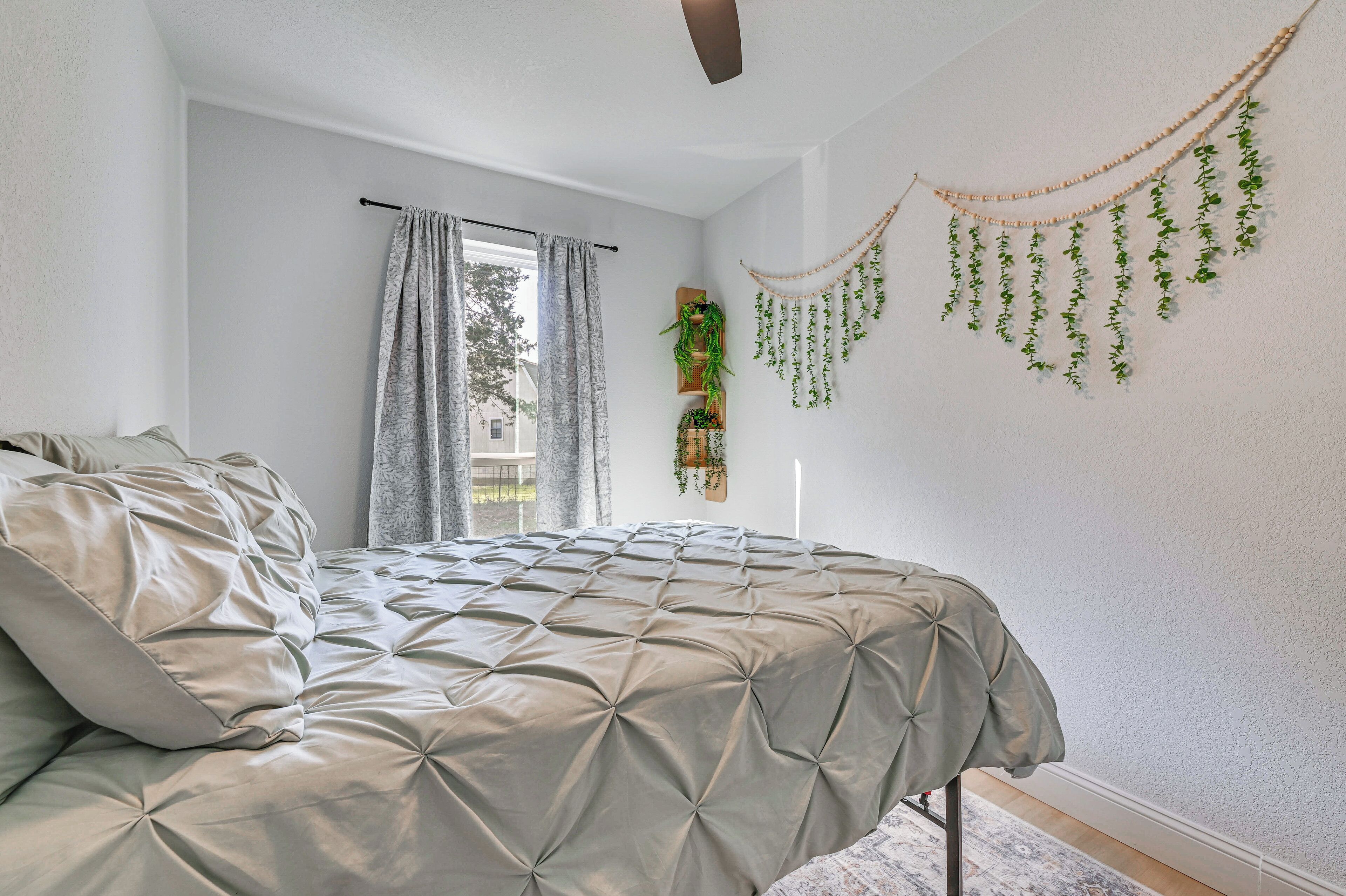 A bedroom with a bed, curtains, a ceiling fan, and wall-mounted plants.