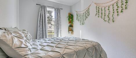 A bedroom with a bed, curtains, a ceiling fan, and wall-mounted plants.