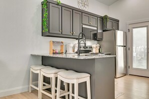 A kitchen with dark grey cabinets, a stainless steel refrigerator, a granite countertop, and two white bar stools. - Bring Your Boat! Family Haven 2 Mi to Lake Texoma (Pottsboro)