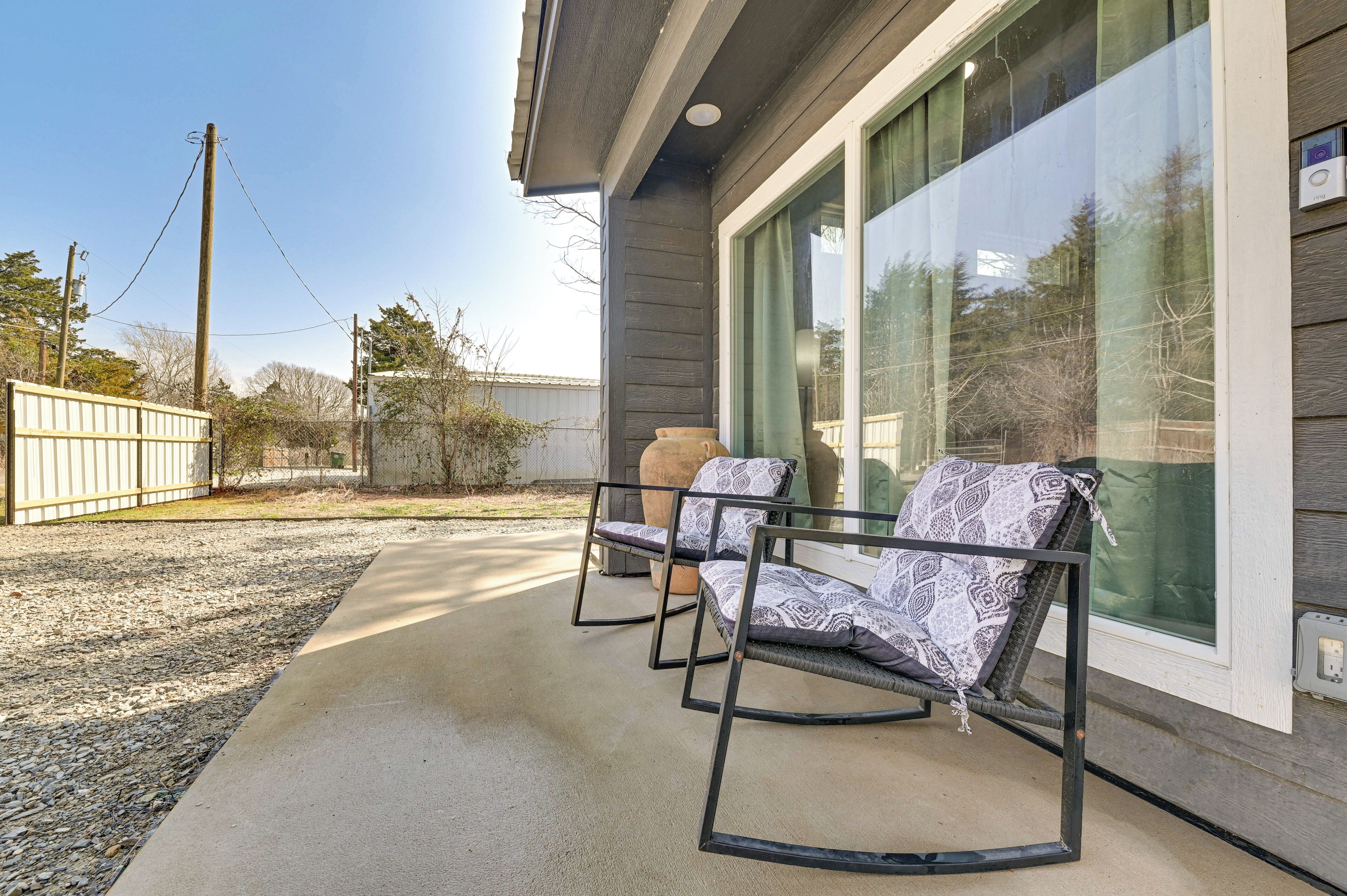 A patio with two rocking chairs, a concrete floor, and a large window with a view of trees and a fence.